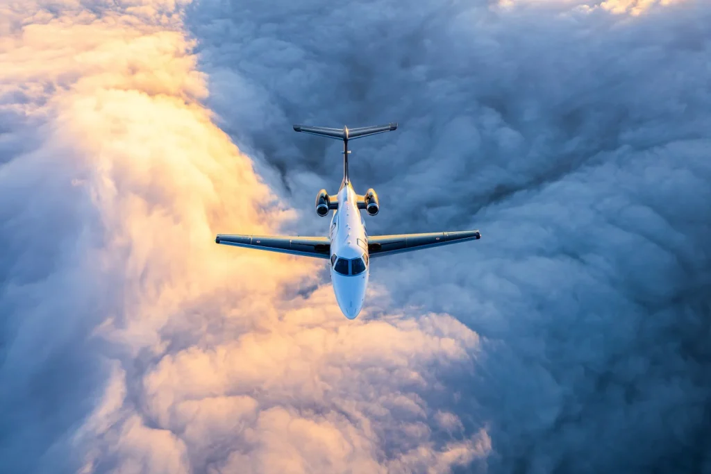 A Embraer Phenom 100 light business jet in flight over sunlit clouds. 