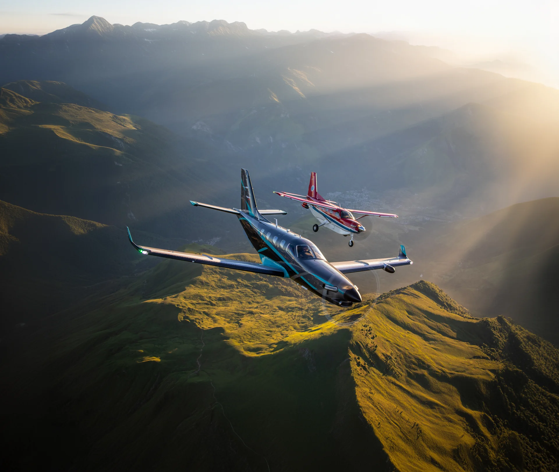 The Daher TBM 960 and the Daher Kodiak 100 is flying in mountainous terrain in beautiful sunlight