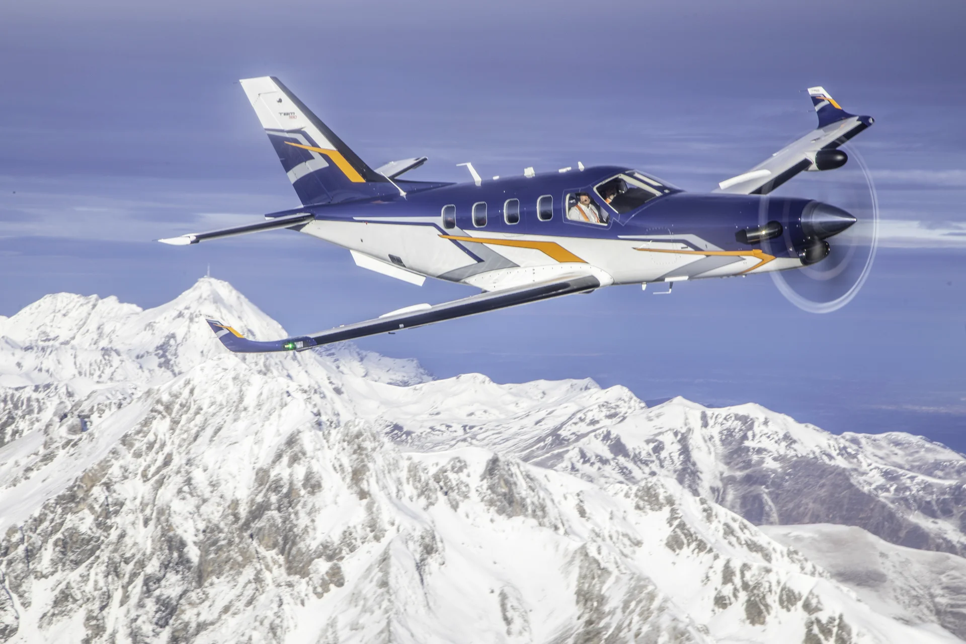 The Daher TBM 980 flying in clear skies over a snow clad mountain ridge. Fly differently!